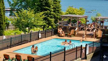 A swimming pool with a wooden deck, lounge chairs, and a view of the lake.