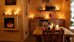A cozy wooden cabin interior with a fireplace, a dining table set with candles, and a kitchen area with a microwave and coffee maker. - Sundowner on Lake George (Lake George)