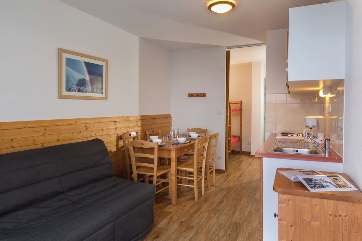 Un espace de vie compact comprenant une table à manger en bois, des chaises, un canapé et un coin cuisine.