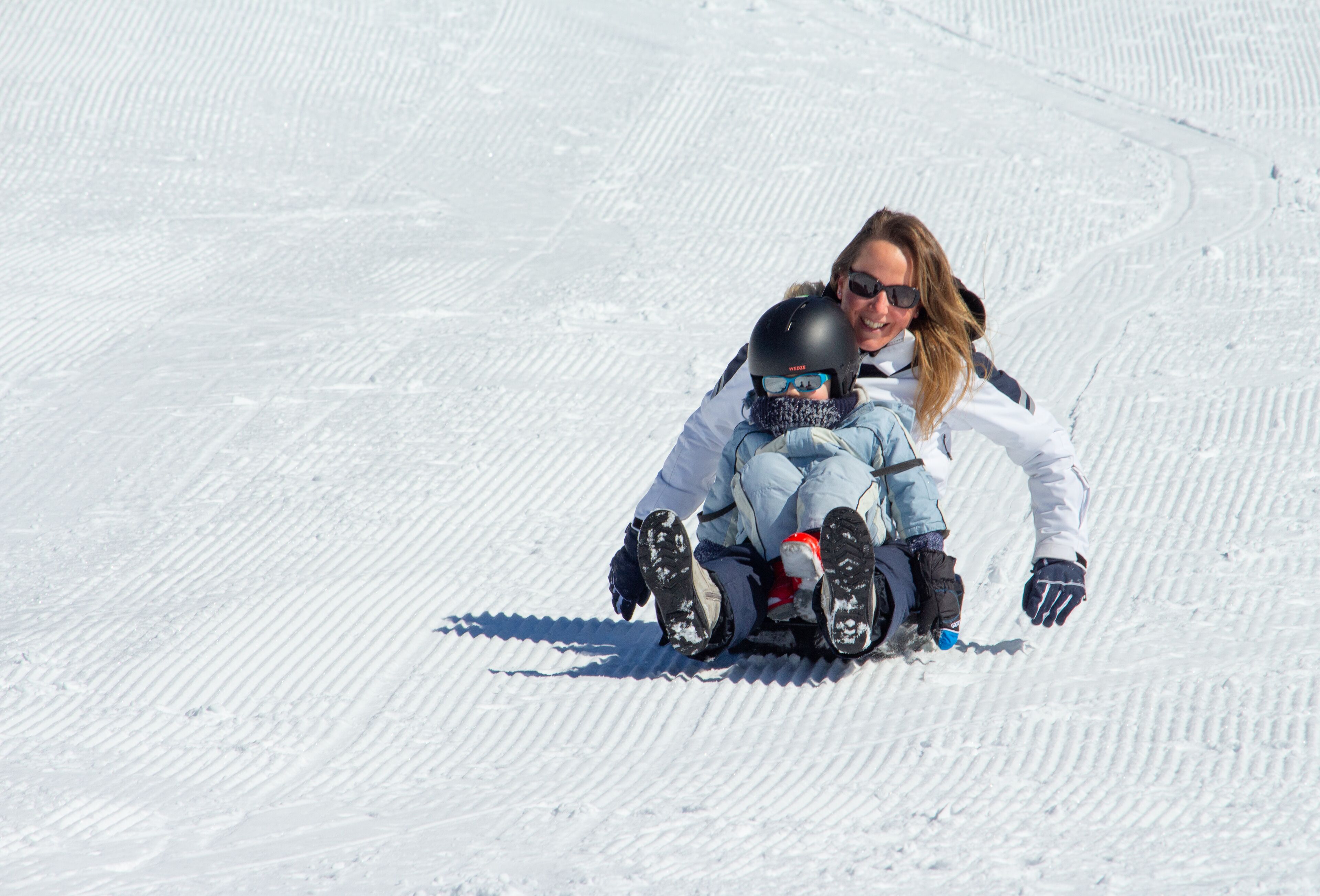 Une pente enneigée où l’on voit une personne et un enfant faire de la luge.