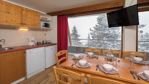 Una cocina con armarios de madera, microondas, lavavajillas y una mesa de comedor para cuatro personas con sillas.