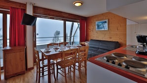 Una cocina acogedora con paredes de madera, una zona de comedor con sillas y una mesa, y un ventanal con cortinas.