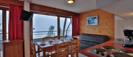 Una cocina acogedora con paredes de madera, una zona de comedor con sillas y una mesa, y un ventanal con cortinas.