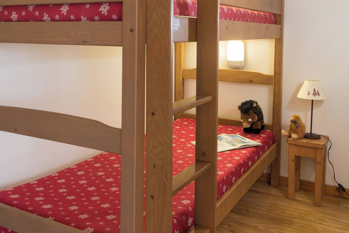 Un lit superposé avec une couvre-lit à motifs rouges, une lampe de chevet et une petite table avec une lampe.