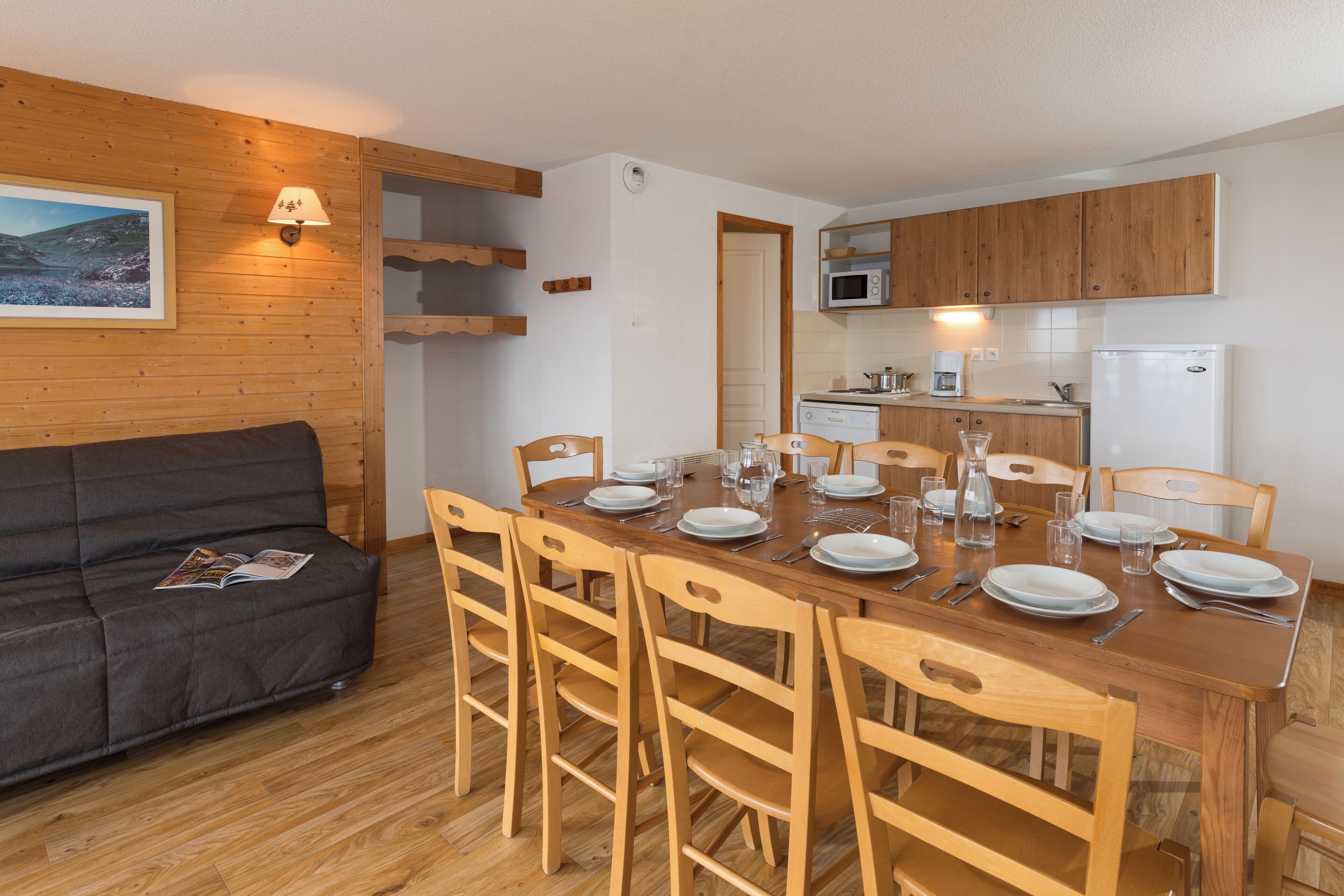 A compact living space with a dining area, kitchenette, and a sofa with a magazine.