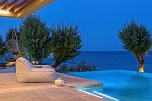 A poolside area with a bean bag chair, a hanging chair, and a small table with two wine glasses.