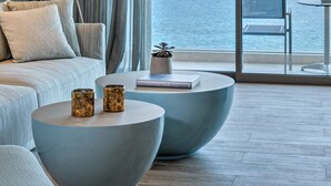 Una sala de estar moderna con un sofá, dos mesas redondas, una lámpara de pie y vistas al mar a través de amplios ventanales.
