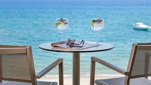 Una mesa con dos vasos de una bebida, un par de gafas y un menú en un balcón con vista al mar.