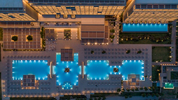 Un hotel moderno con varias piscinas, zonas de estar al aire libre y una terraza en la azotea bien iluminada.