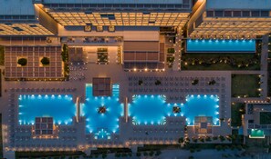 Un hotel moderno con varias piscinas, zonas de estar al aire libre y una terraza en la azotea bien iluminada.