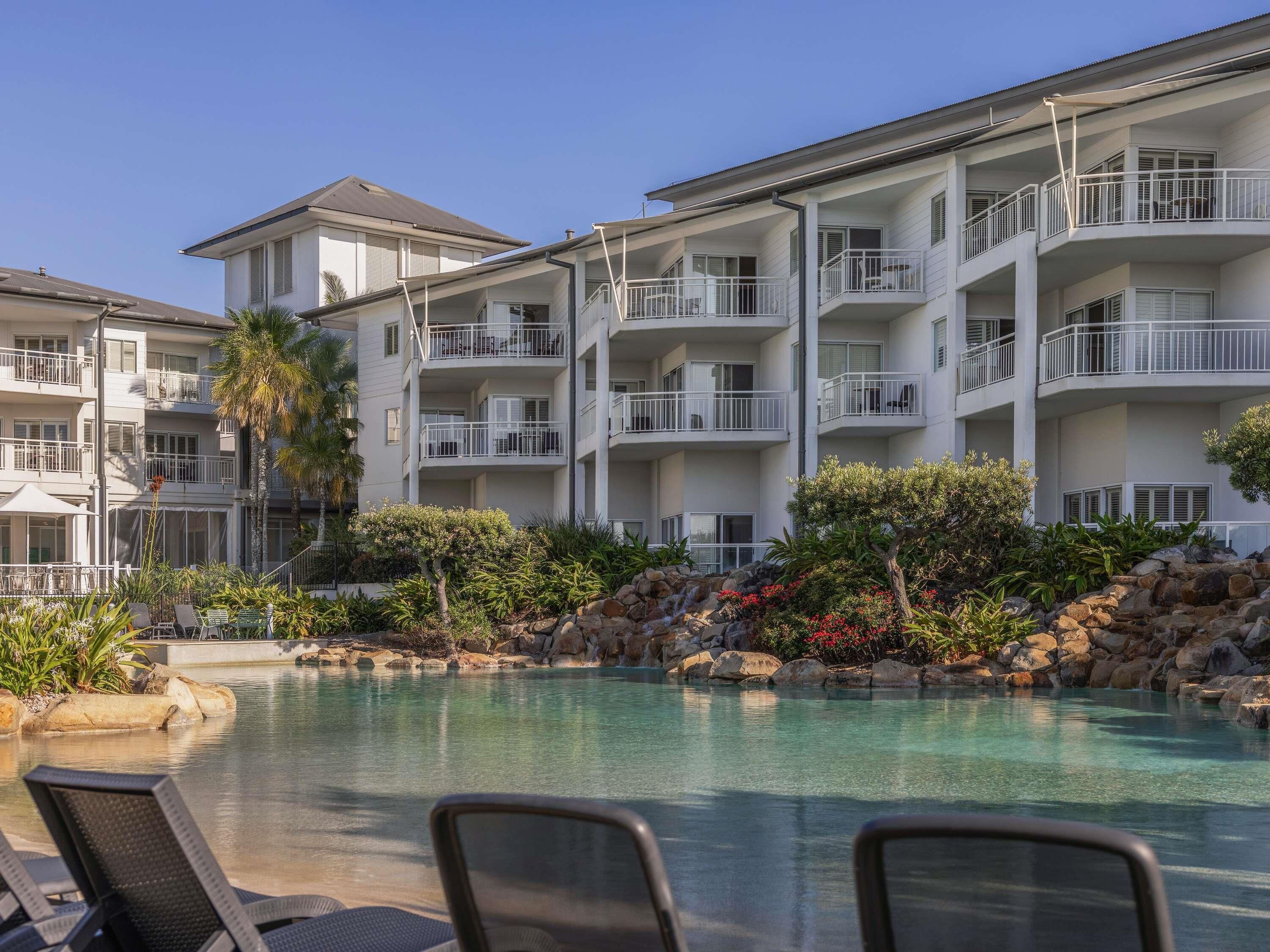 A hotel with multiple balconies, a swimming pool, and a landscaped garden.