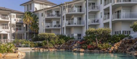 A hotel with multiple balconies, a swimming pool, and a landscaped garden.