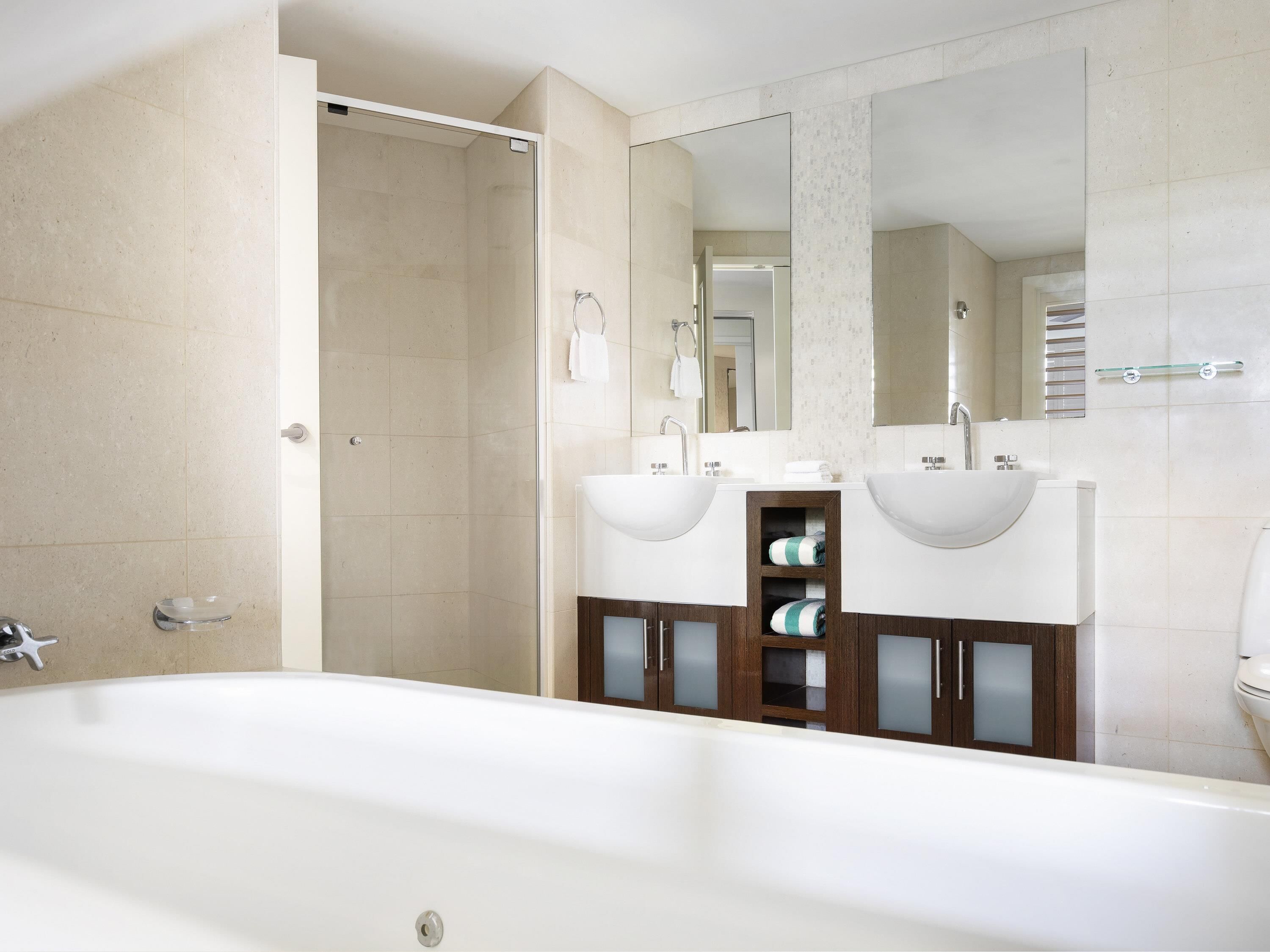 Une salle de bain moderne avec une baignoire, deux lavabos, une douche en verre et un grand miroir.