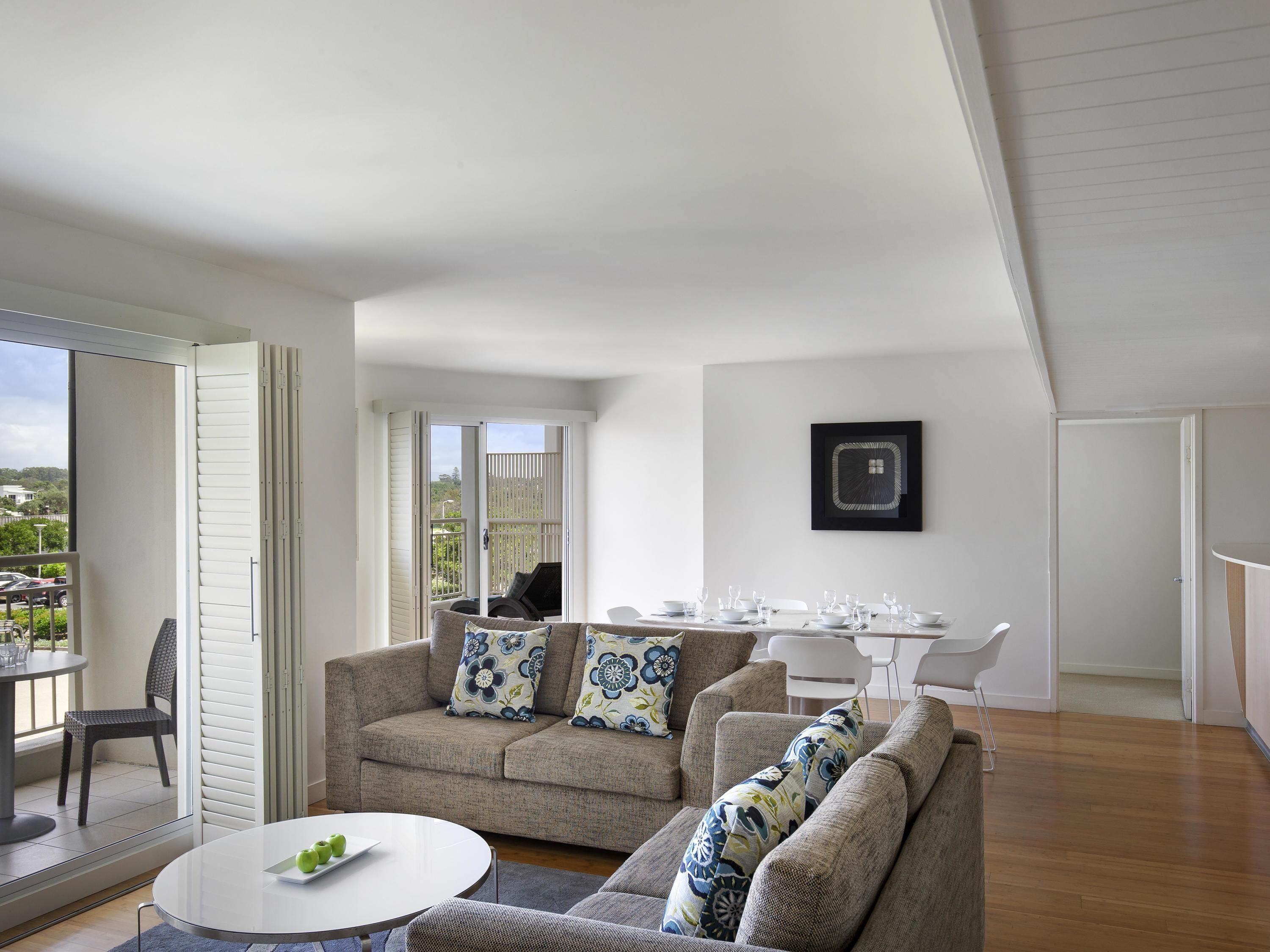 A modern living room with a sofa, a dining table set for six, and a balcony with a view.