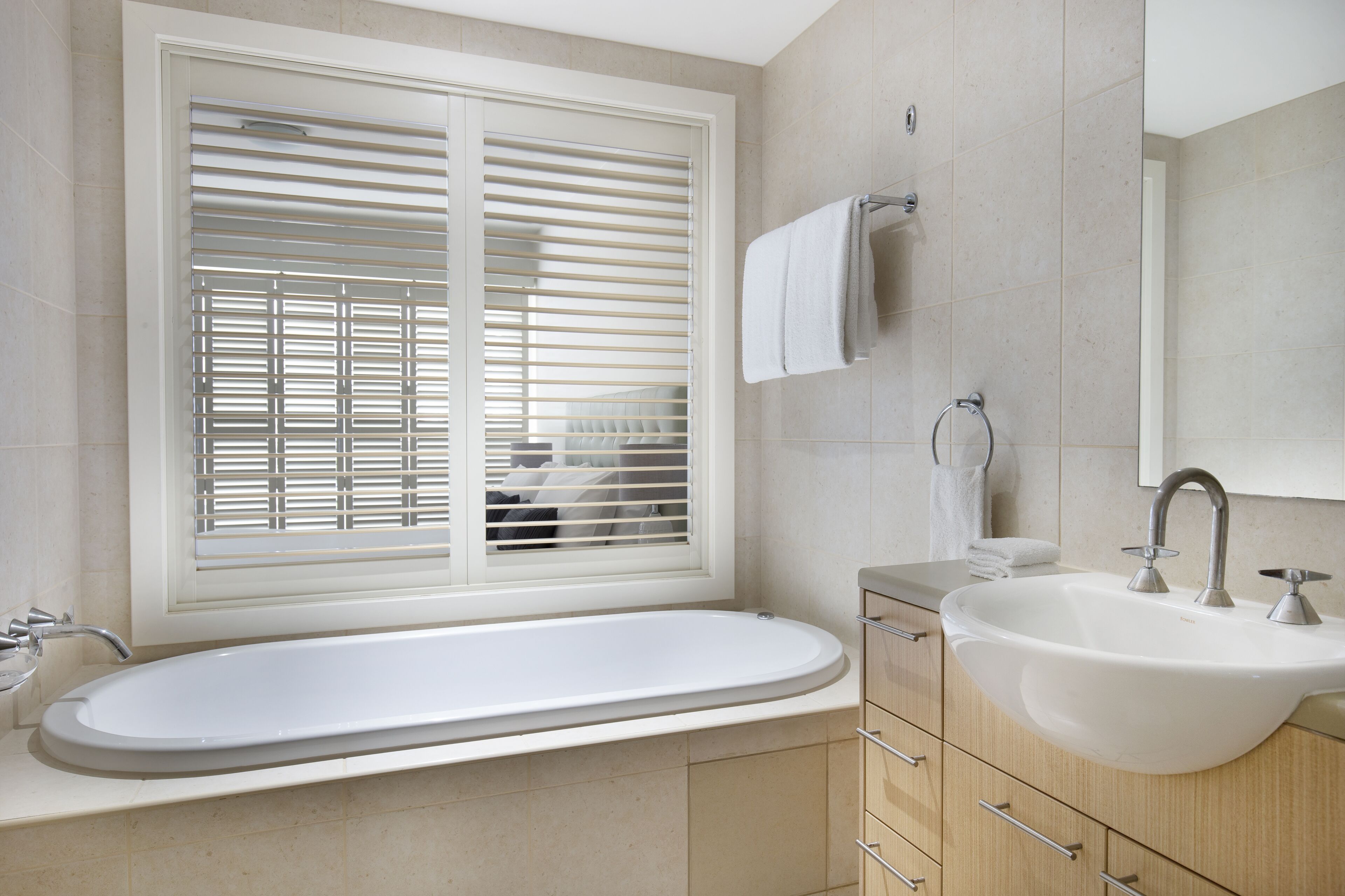 Un baño moderno con una bañera independiente, un lavamanos y un ventanal con persianas.
