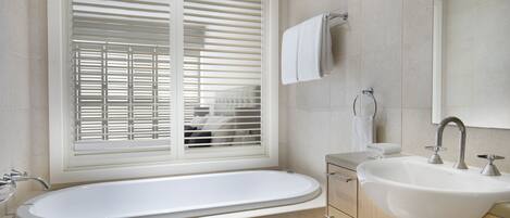 Un baño moderno con una bañera independiente, un lavamanos y un ventanal con persianas.