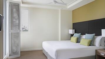 A hotel room with a bed, a nightstand, a ceiling fan, and a window with blinds.