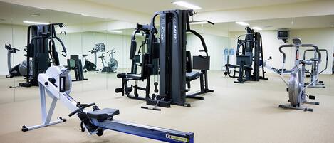 A gym with various exercise machines, including a rowing machine, a leg press, and a stationary bike.