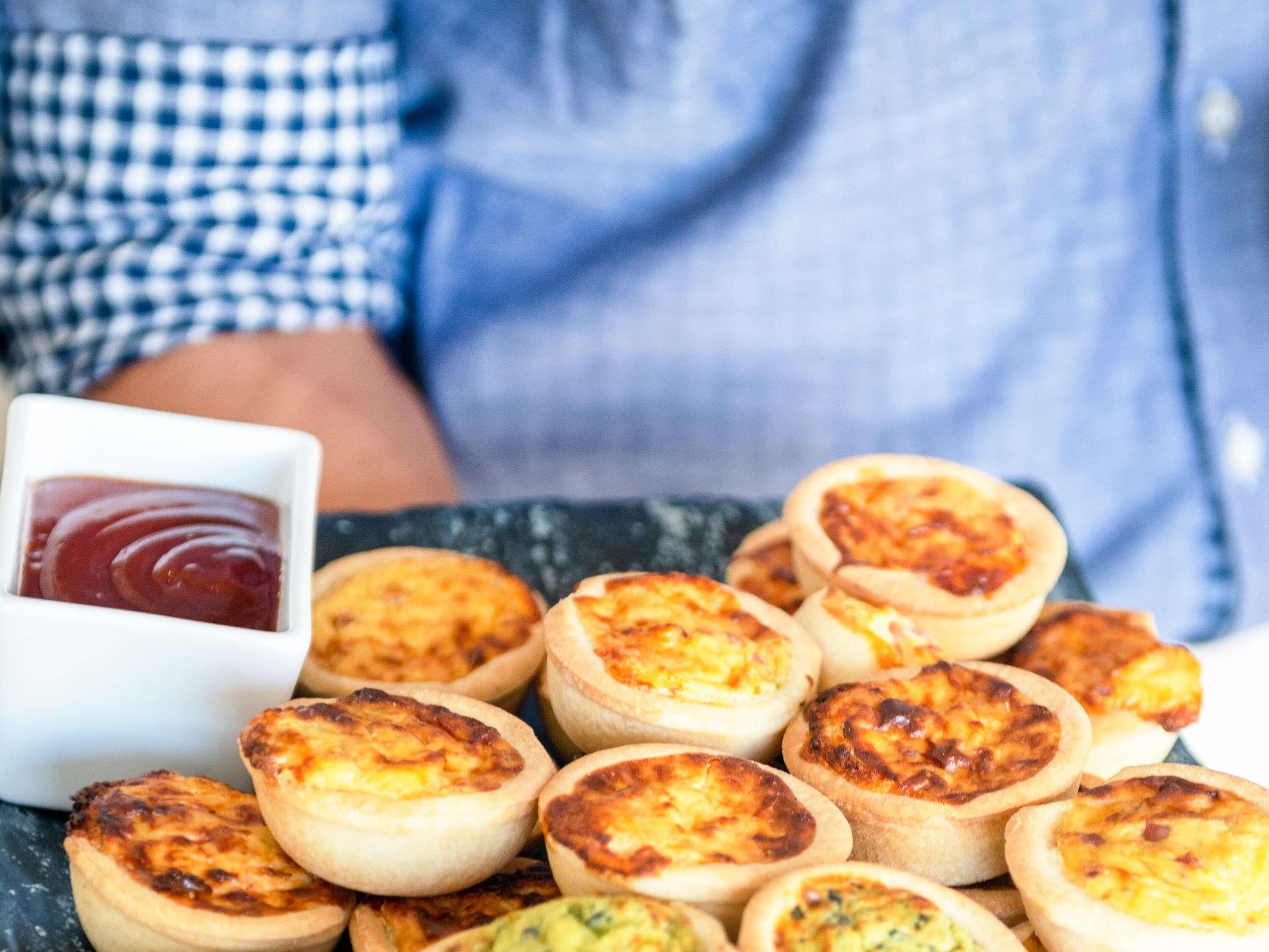 A person holding a plate of mini quiches with a small bowl of ketchup.