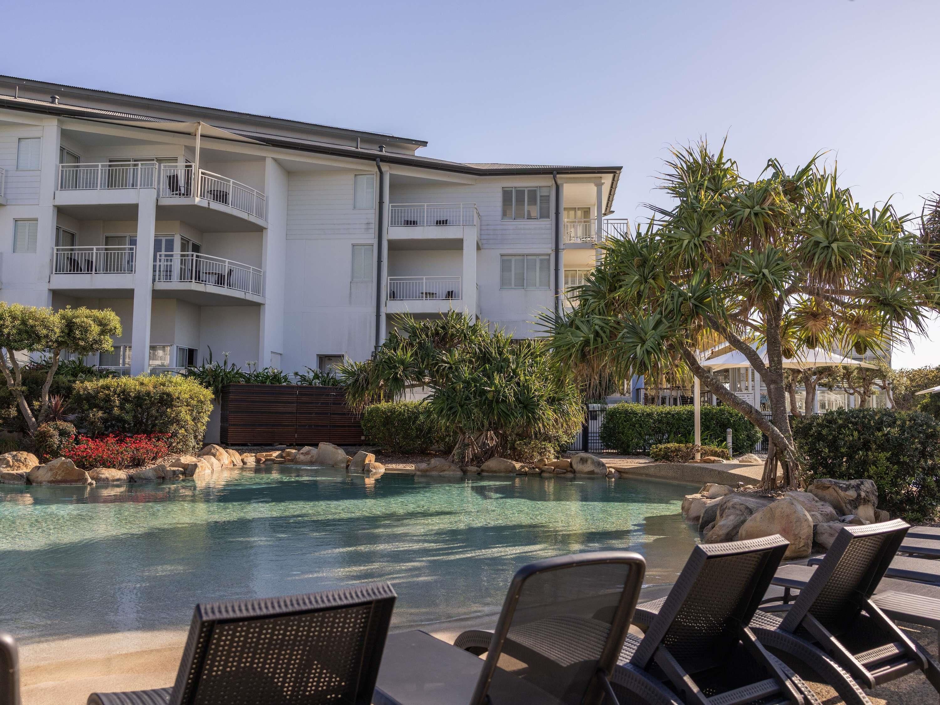 A hotel with a swimming pool, lounge chairs, and a landscaped garden.