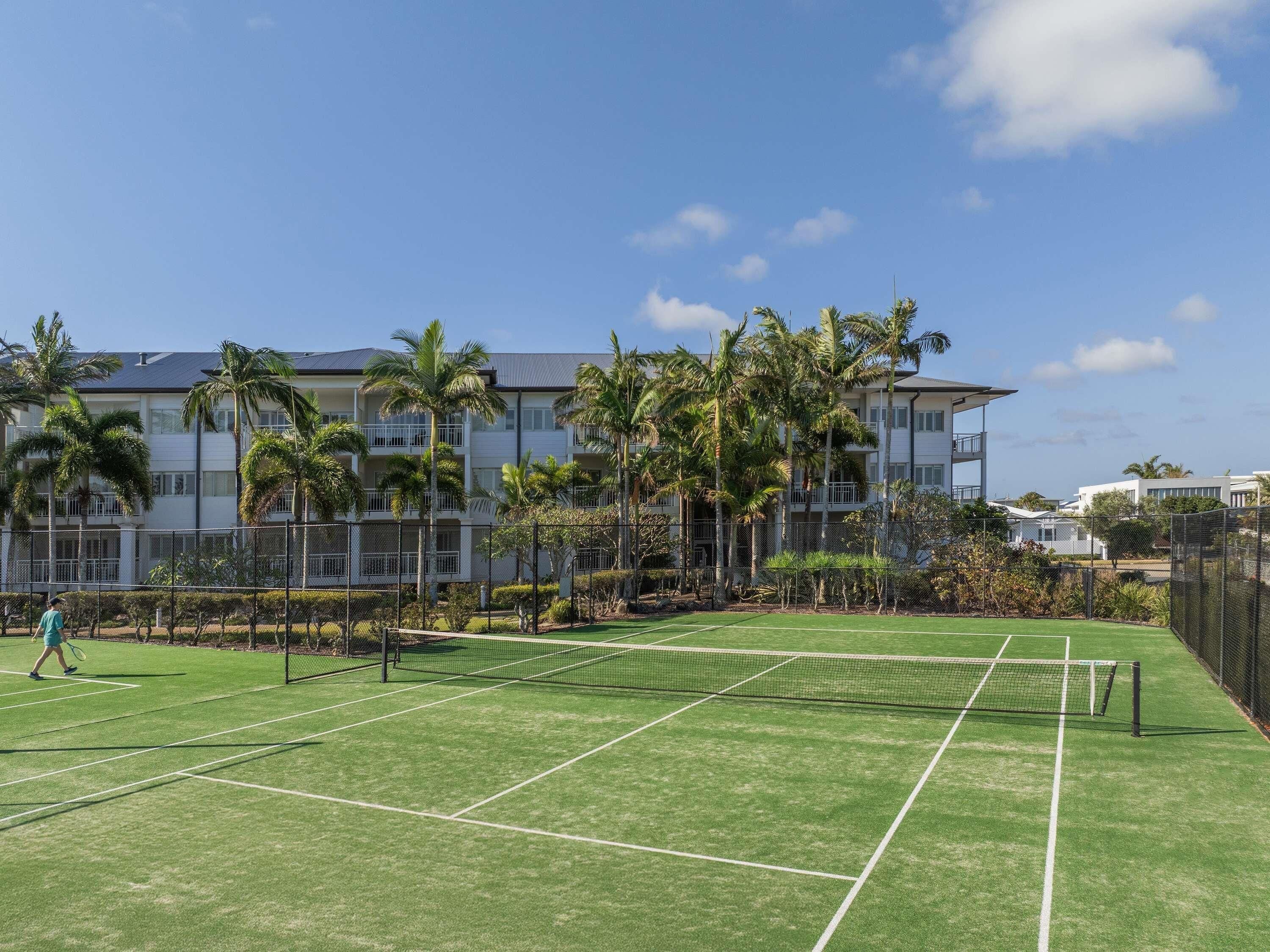 A tennis court with a net, surrounded by a fence, and palm trees.