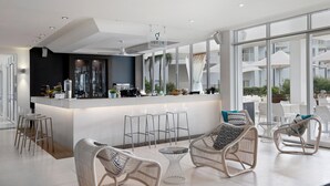 A modern bar area with a white counter, bar stools, wicker chairs, and large windows offering views of the outdoors. - Mantra on Salt Beach (Kingscliff)