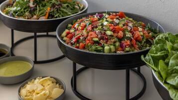 Ein Buffet mit verschiedenen Speisen, darunter Salate, eine Käseschale und eine Dressing-Schale.
