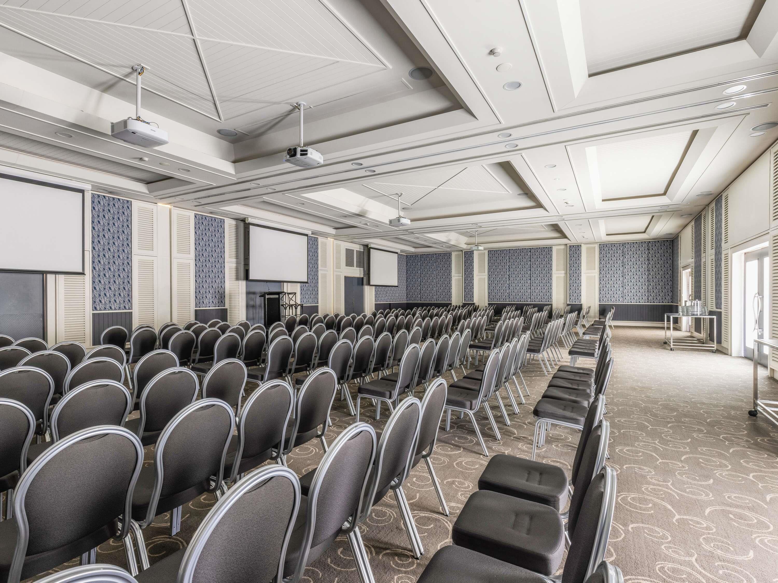 A conference room with rows of chairs, a projector, and a screen.