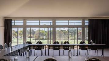 A conference room with a long table, chairs, and a view of a sports field through large windows.