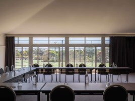 A conference room with a long table, chairs, and a view of a sports field through large windows.