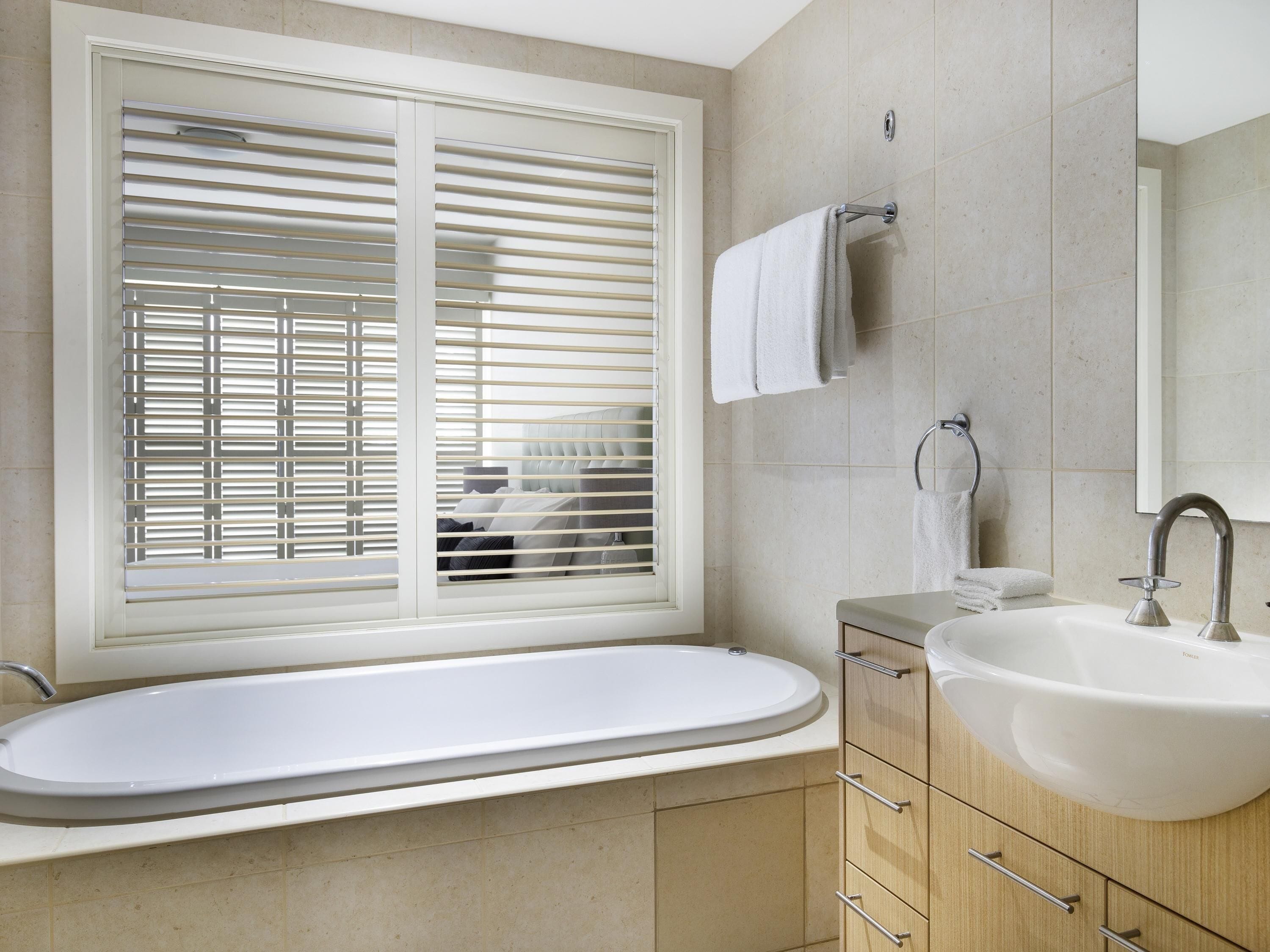 A bathroom with a bathtub, a sink, a window with blinds, and a towel rack.