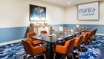 A conference room with a long table, orange chairs, a projector screen, and a large abstract painting.