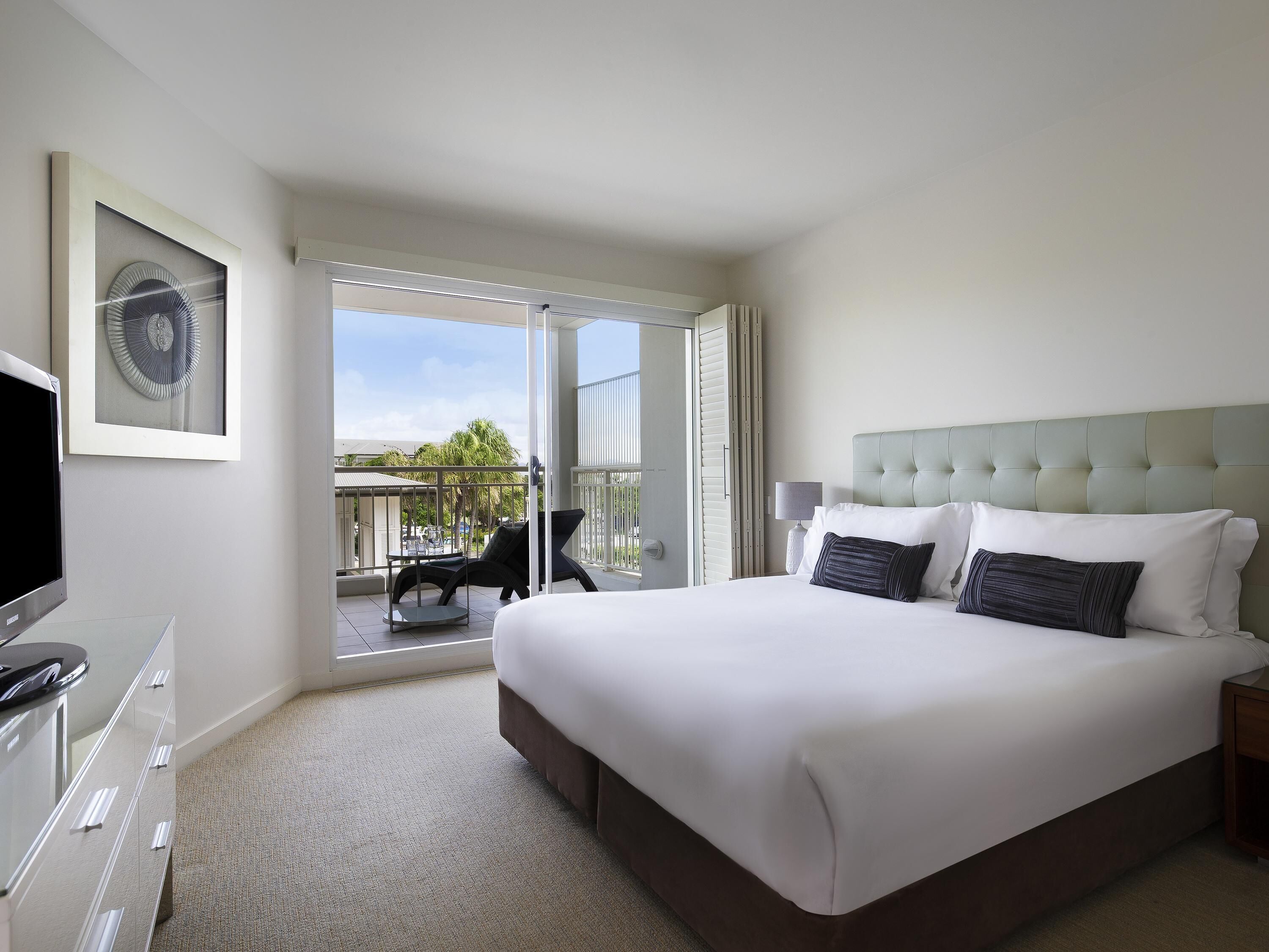 Une chambre d’hôtel avec un grand lit, une télévision, un balcon avec une chaise et un tableau encadré au mur.