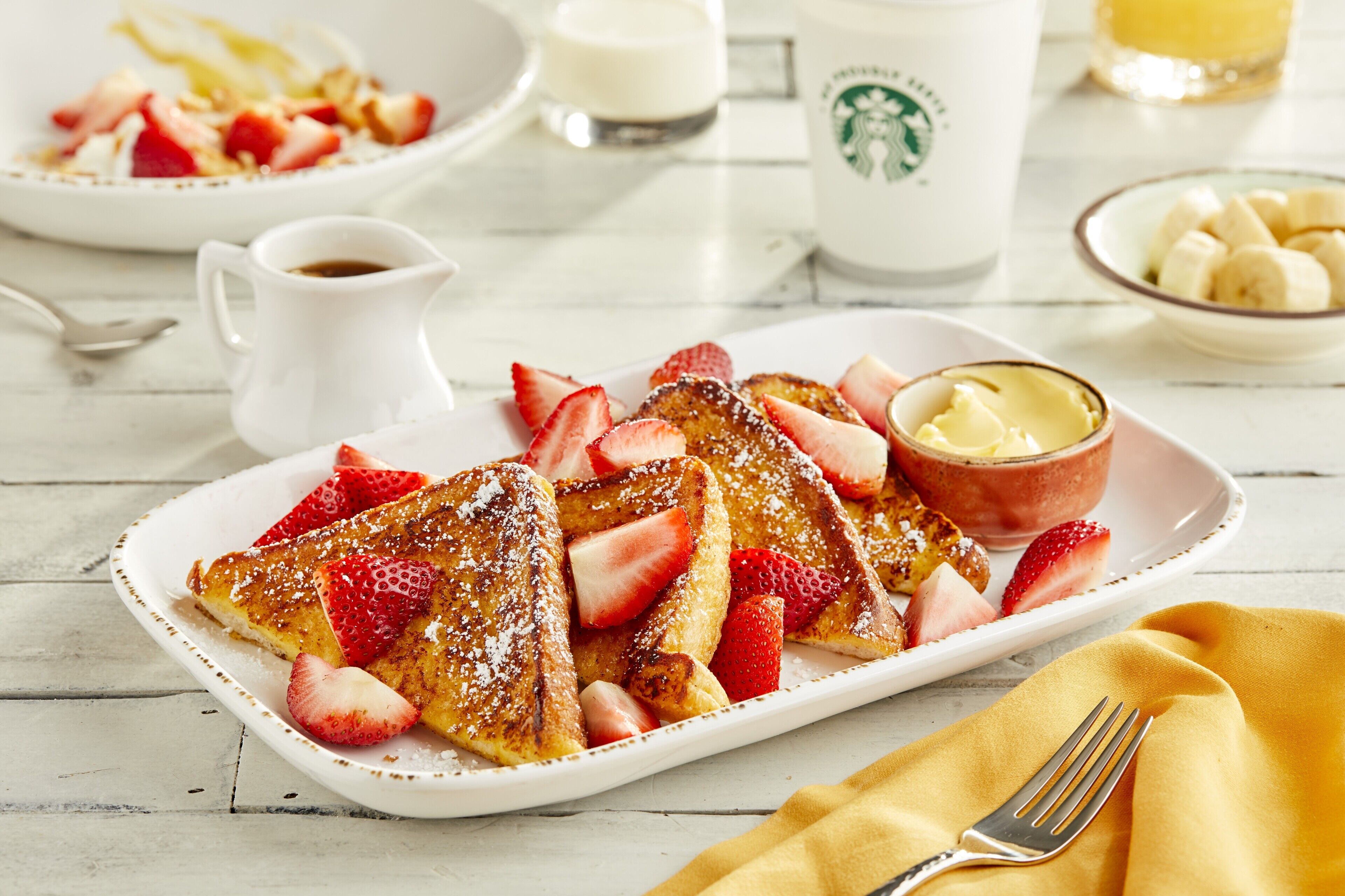 A breakfast plate with French toast, strawberries, and a small bowl of butter.