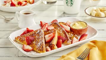 A breakfast plate with French toast, strawberries, and a small bowl of butter.