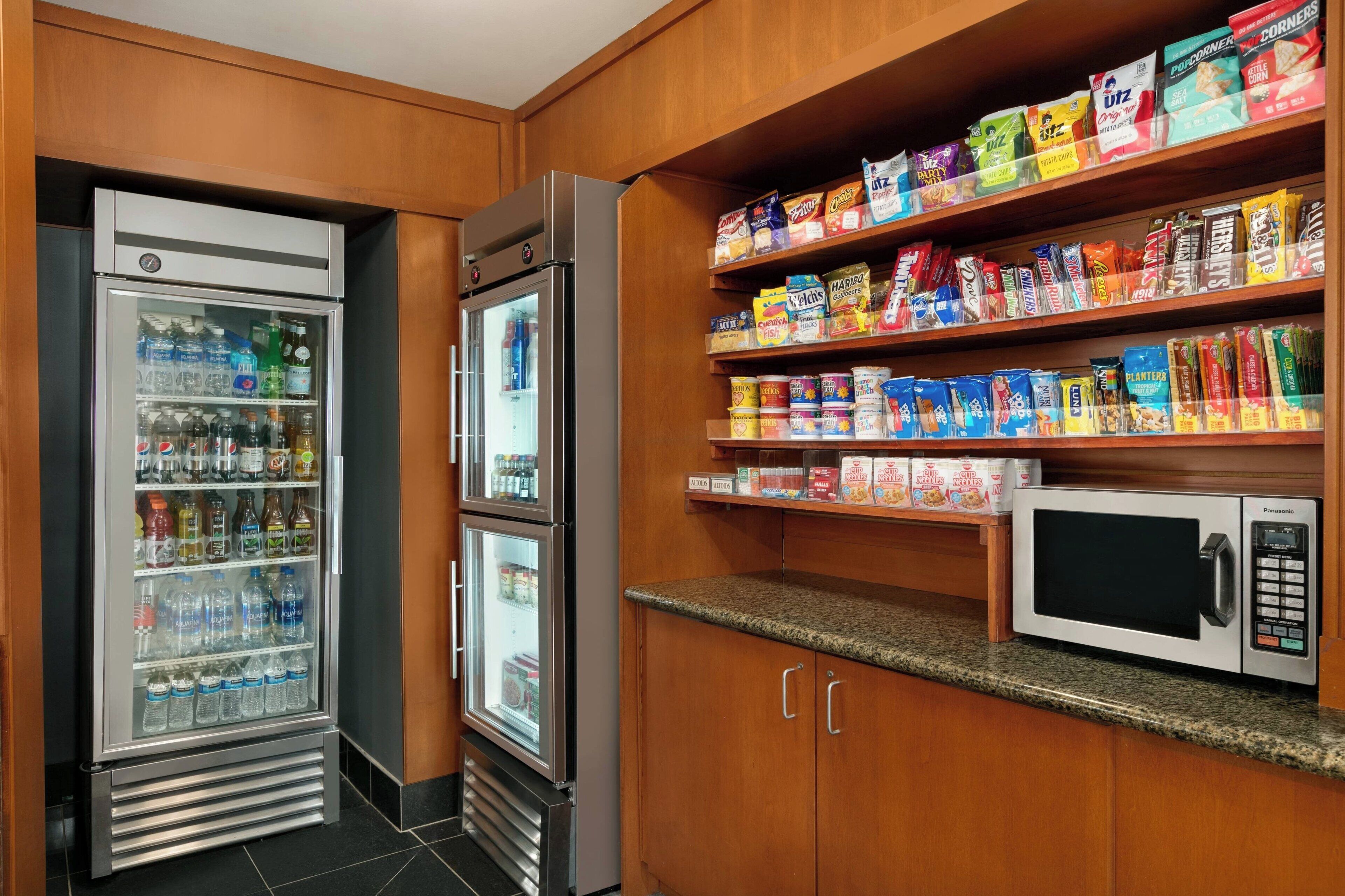 A kitchenette with a refrigerator, a microwave, and shelves stocked with snacks and beverages.