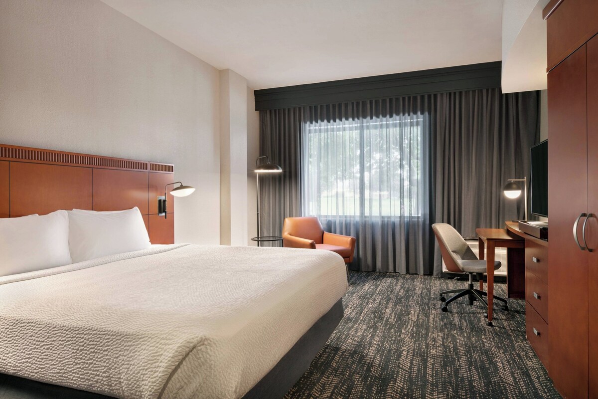 A hotel room with a large bed, a desk, a chair, and a television.