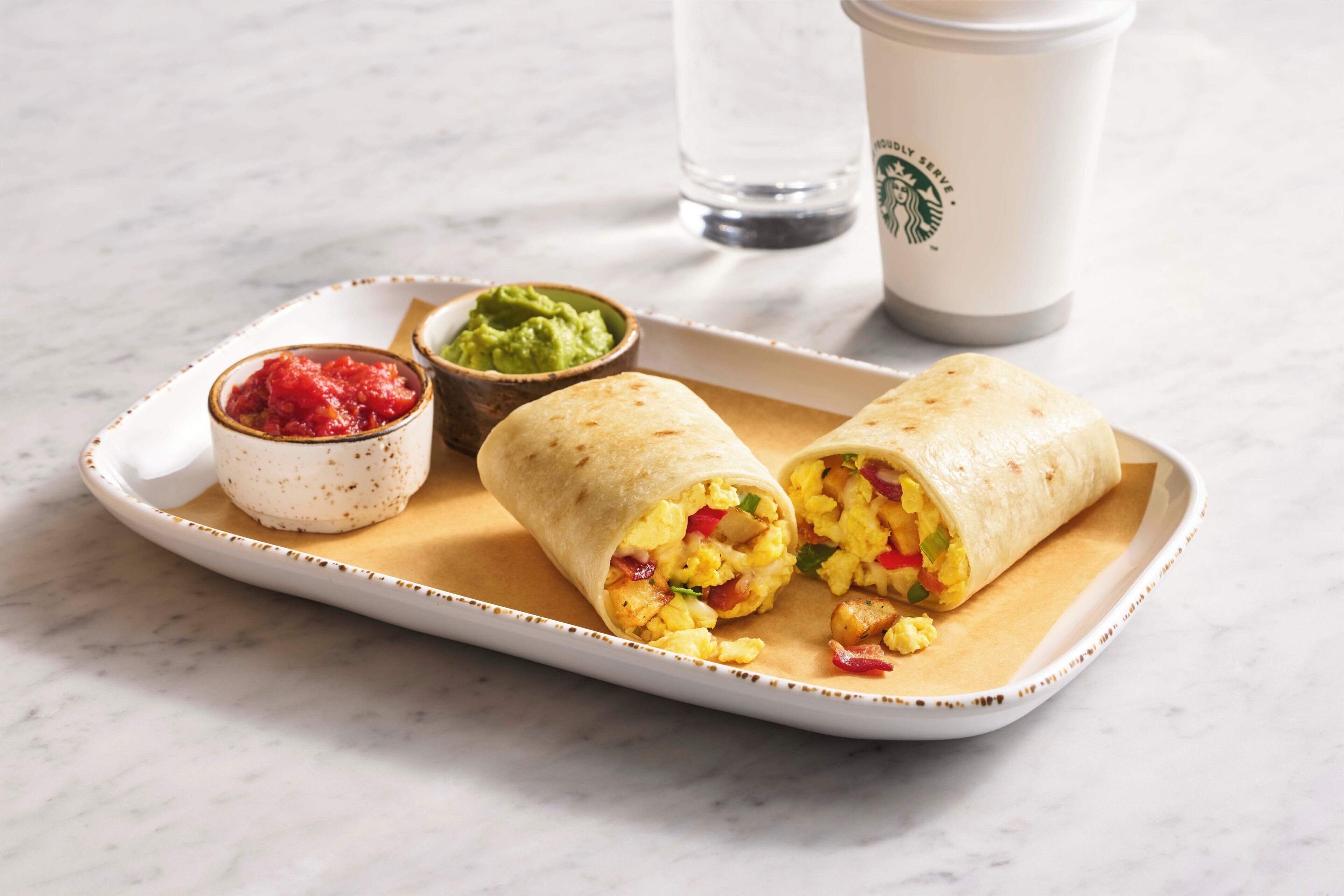 A tray with two burritos, a small bowl of guacamole, and a bowl of salsa.