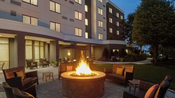 A courtyard with a central fire pit surrounded by wicker furniture, a building with multiple windows in the background, and a well-maintained lawn. - Courtyard by Marriott Lancaster (Lancaster)