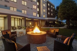 A courtyard with a central fire pit surrounded by wicker furniture, a building with multiple windows in the background, and a well-maintained lawn. - Courtyard by Marriott Lancaster (Lancaster)