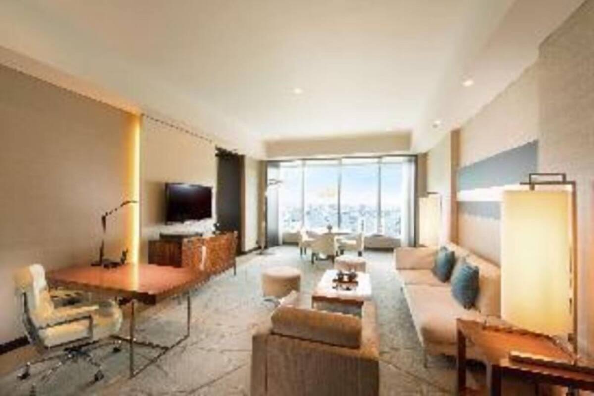 Habitación de hotel con un ventanal grande, un televisor de pantalla plana, un sofá, una mesa de centro y un escritorio con una silla.