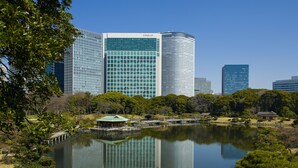 A modern cityscape with high-rise buildings, including a prominent CONRAD building, and a serene park with a lake and traditional Japanese structures. - Conrad Tokyo (Tokyo)