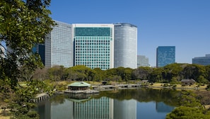 A modern cityscape with high-rise buildings, including a prominent CONRAD building, and a serene park with a lake and traditional Japanese structures. - Conrad Tokyo (Tokyo)