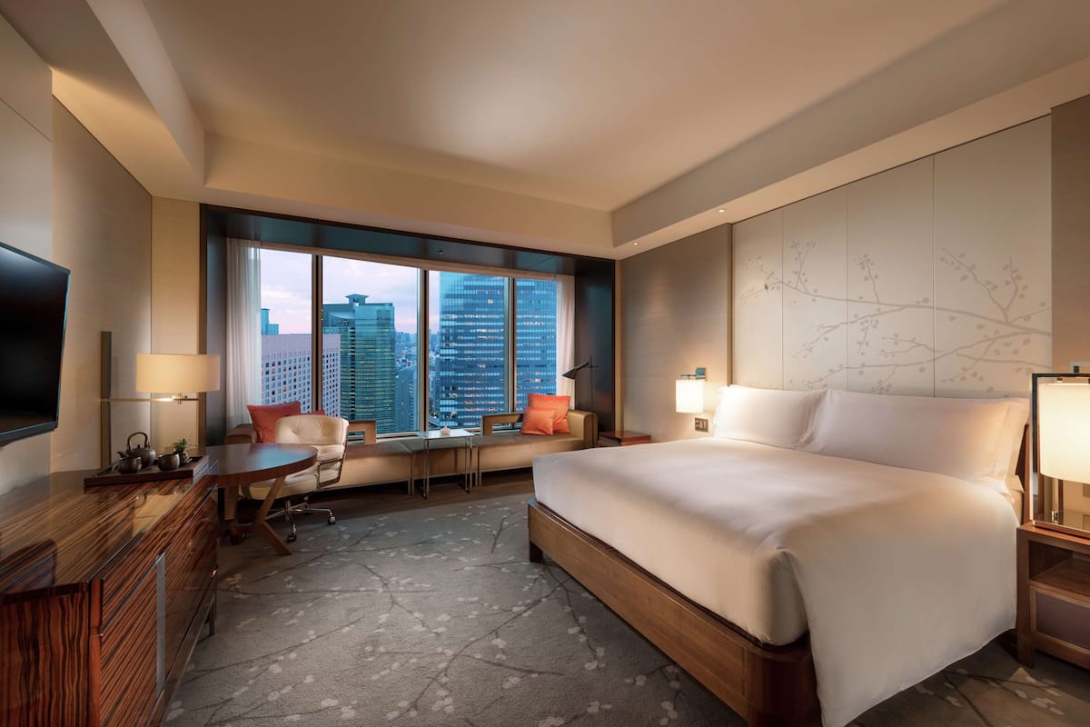 Habitación de hotel con una cama grande, un escritorio, una silla, un televisor y vistas a la ciudad.
