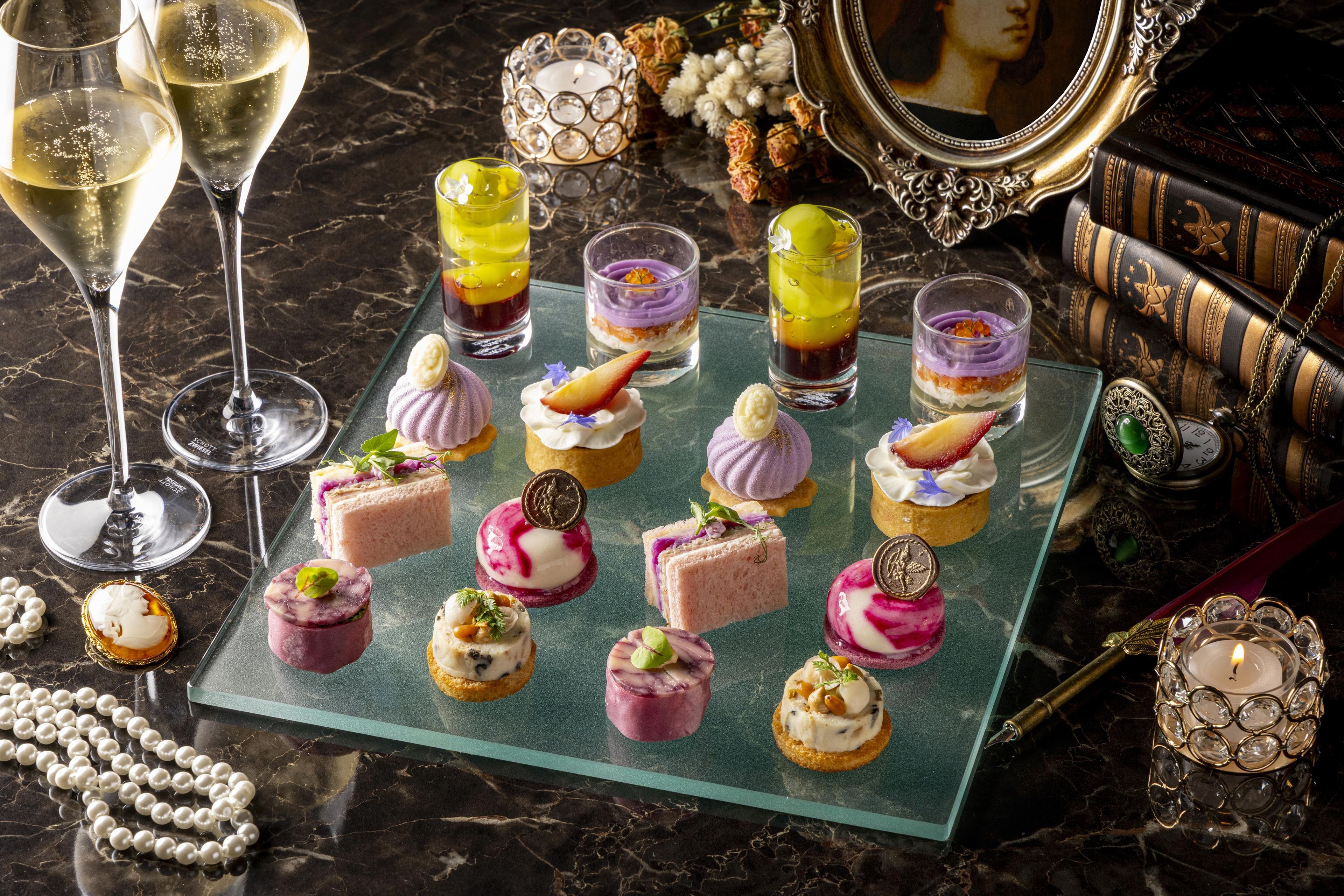 A selection of gourmet desserts on a glass platter, accompanied by two glasses of white wine, set on a marble surface with decorative elements.