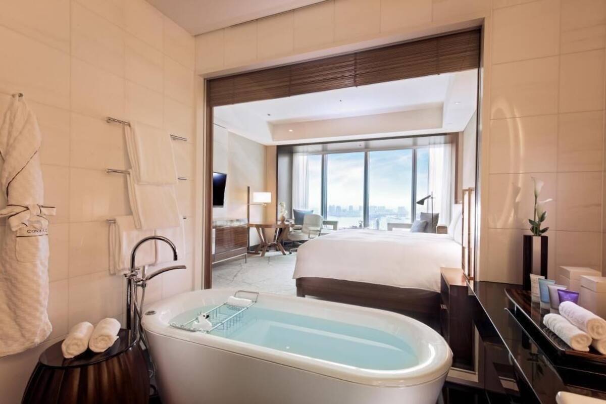 Habitación de hotel con bañera, cama, escritorio y un amplio ventanal.