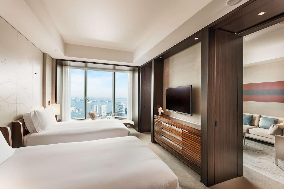 Habitación de hotel moderna con dos camas, un televisor grande y vistas a la ciudad.