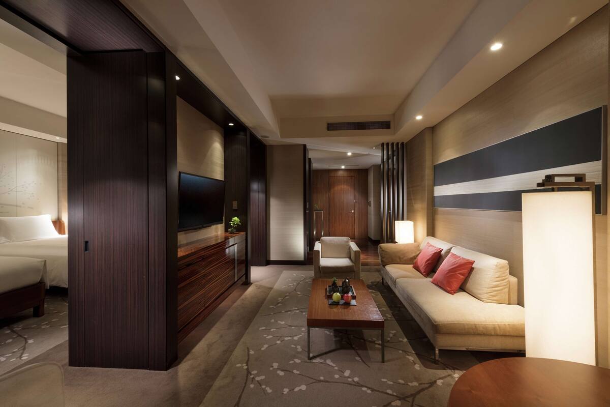 A modern hotel room with a sofa, a TV, a coffee table, and a bed.