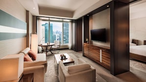 A modern hotel room with a large window, a flat-screen TV, a sofa, a coffee table, and a bed. - Conrad Tokyo (Tokyo)