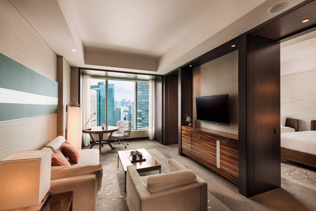 Habitación de hotel moderna con un ventanal grande, televisor de pantalla plana, sofá, mesa de centro y cama.
